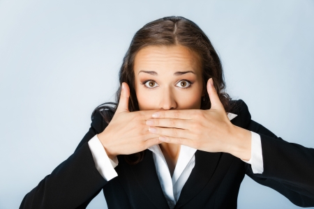 Portrait of surprised excited young business woman covering with hands her mouth, over blue backgroundの写真素材