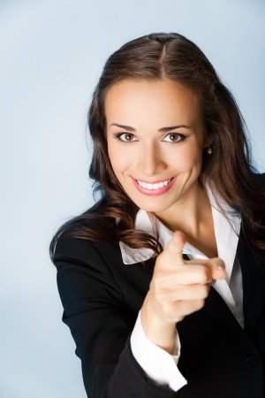 Portrait of young smiling business woman pointing finger at viewer, over blue backgroundの写真素材