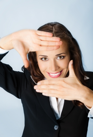 Portrait of young happy smiling business woman framing her face with hands, over blue backgroundの写真素材