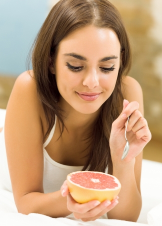 Portarit of young woman eating grapefruit at homeの写真素材