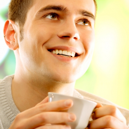 Young happy smiling man with cup of coffee, outdoorsの写真素材