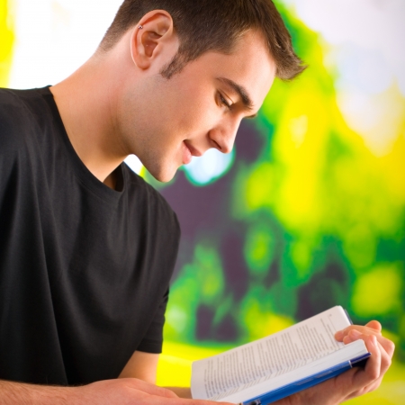 Young happy man reading book or textbook, outdoorの写真素材