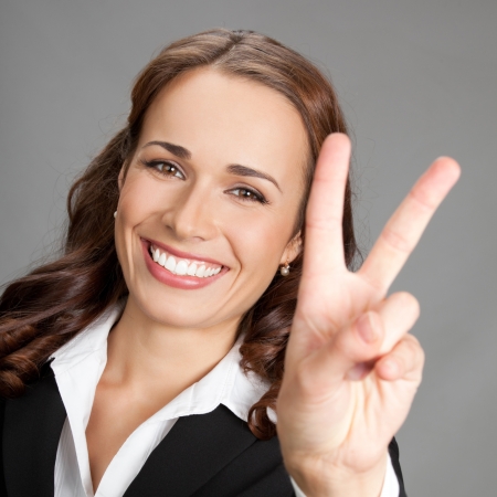 Happy smiling beautiful young business woman showing two fingers or victory gesture, over gray backgroundの写真素材