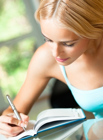 Young beautiful blond woman studying with notebook or organiser, indoorsの写真素材