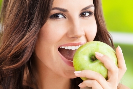 Portrait of young woman eating green apple, outdoorsの写真素材