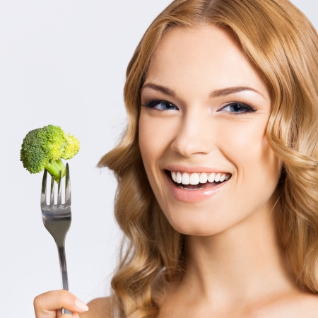 Portrait of happy smiling young beautiful woman eating broccoli, over gray backgroundの写真素材