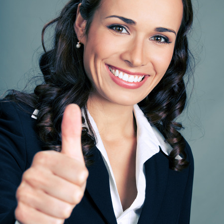 Happy smiling business woman showing thumbs up gesture, over grey backgroundの写真素材