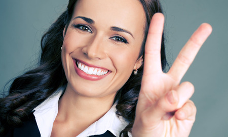 Happy smiling beautiful young business woman showing two fingers or victory gesture, over gray backgroundの写真素材