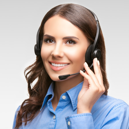Portrait of smiling cheerful customer support phone operator in headset, against grey backgroundの写真素材