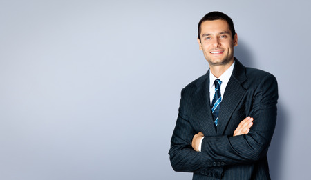 Happy smiling businessman with crossed arms pose, with blank copyspace area for text or slogan, against grey background