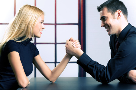 Young happy couple or business people fighting in arm-wrestlingの写真素材