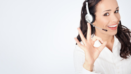 Portrait of happy smiling cheerful customer support phone operator in headset showing okay gesture, against grey background, with copyspaceの写真素材