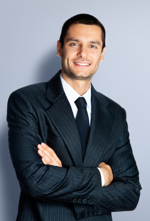 Portrait of cheerful young businessman with crossed arms pose, against grey backgroundの写真素材