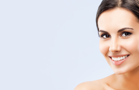 Portrait of beautiful young happy smiling brunette woman, with naked shoulders, over grey background, with empty blank copyspace area for slogan or textの写真素材