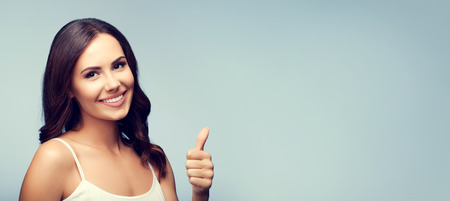 Portrait of beautiful smiling young brunette woman showing thumb up gesture, with blank copyspace area for text or sloganの写真素材