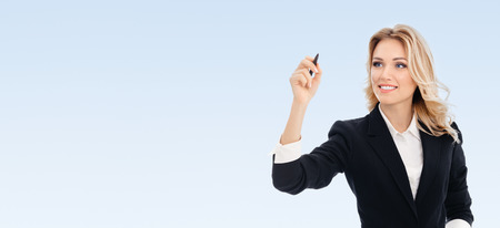 Happy smiling cheerful young businesswoman writing or drawing something on screen or transparent glass, by blue marker, on blue background, with blank copyspace area for text or sloganの写真素材