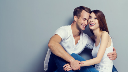 Portrait of beautiful young couple, looking at each other with smile. Caucasian models - love, relationship, dating, happy lovers, concept shot, against grey, with copyspace for slogan or text message.  Horizontal banner composition.の写真素材