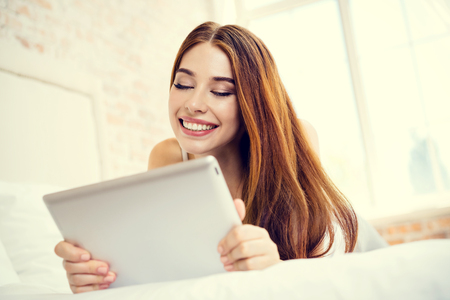 Cheerful young woman using no-name tablet computer, at homeの写真素材