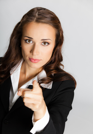 Portrait of young serious businesswoman pointing finger at viewer, over grey background. Business success concept.の写真素材
