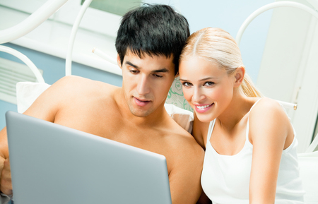 Young happy smiling couple working with laptop at bedroomの写真素材