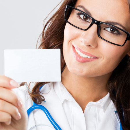 Portrait of happy smiling young female doctor showing blank business card or invitation, over grey backgroundの写真素材