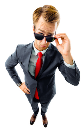 Are you seriously?! Full body portrait of funny skeptic young businessman in black confident suit and red tie, looking through sunglasses, top angle view shot, isolated against white background. Business concept.の写真素材