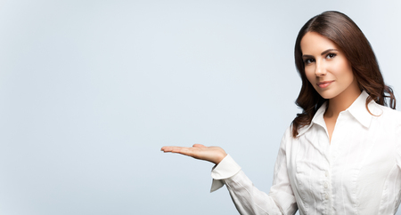 Happy smiling young cheerful businesswoman, showing something or blank copyspace area for slogan or text message, on grey background, with blank copyspace area for slogan or text. Success in business concept studio shot. の写真素材