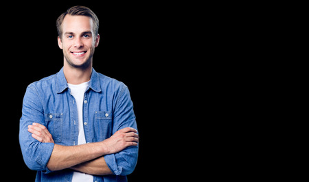 Portrait of happy smiling man standing in crossed arms pose, with empty copy space area for some slogan, advertising or text message, over black background. Caucasian male model in smart casual clothing, studio shoot.の写真素材