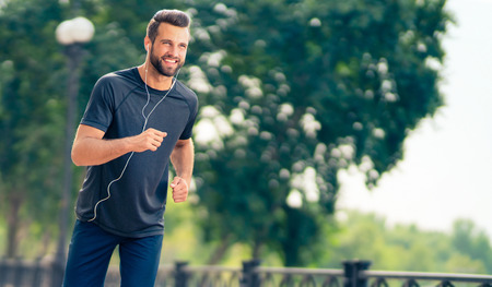 Young happy cheerful smiling man, during morning jogging outdoors. Fitness, sport, exercising and workout in city concept.の写真素材
