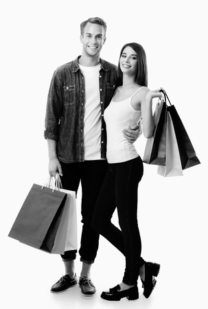 Happy couple with shopping bags, standing close to each other and looking at camera with smile. Love, holiday sales, shop, retail, consumer concept. Black and white.の写真素材