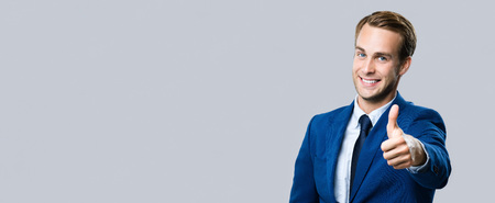 Portrait of happy smiling businessman showing thumbs up gesture, over grey background. Business success concept. Blank copy space area for some advertisiment, slogan or text.の写真素材