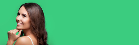 Portrait of thinking happy smiling young beautiful woman looking up, in white casual clothing, over green background, with big copy space area, for some text, advertising or sloganの写真素材