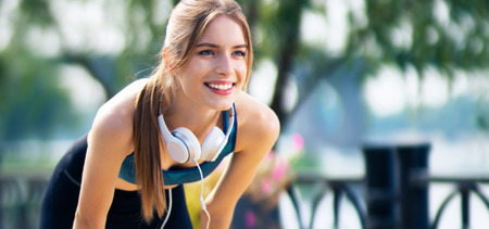 Image of young woman in fit wear and headphones tired, during morning jogging outdoors, with smile. Fitness, sport, exercising and workout in city concept.の写真素材