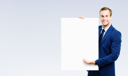 Bright image of businessman showing blank signboard, over grey background. Empty copyspace area for slogan or advertising text message. Success in business, job and education concept studio shot.の写真素材