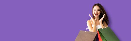 Shopping woman. Happy excited girl, holding bags, isolated over violet purpure color background. Copy space for some slogan or sign text. Consumerism and sales ad concept photo. Banner composition.の写真素材