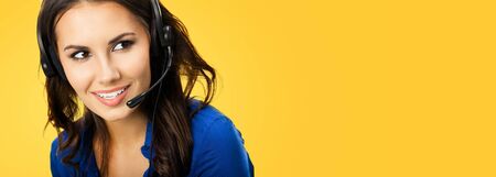 Call center service. Customer support phone sales female operator with copy space area for some text or slogan, over yellow orange color background. Beautiful woman in headset.の写真素材