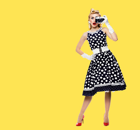 Full body portrait of young woman with noname old film camera, taking picture, dressed in pin up...