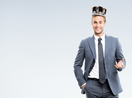 I am business king! Portrait of happy smiling young businessman in grey confident suit and crown,...
