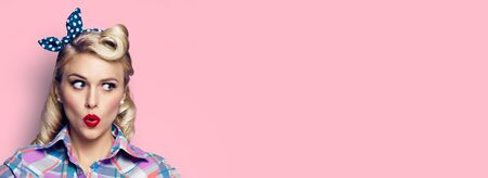 Excited surprised woman. Girl in pin up style, looking sideways. Retro fashion and vintage concept. Pink rose color background. Copy space for some text.の写真素材