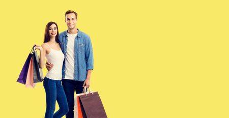 Love, holiday sales, shop, retail, consumer concept - happy couple with shopping bags, standing close to each other, and looking at camera. Yellow color background.の写真素材