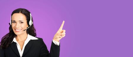 Call center service. Customer support female phone sales operator in headset showing something or copy space for some text, imaginary, product or slogan, over violet purple background.の写真素材