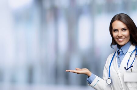 Portrait of female doctor showing, holding or giving something or some product or drug, copy space for slogan or sign text, blurred office background. Brunette woman at healthcare medic concept.の写真素材