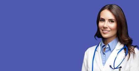 Portrait picture of happy smiling female doctor in white uniform coat and stethoscope, standing over dark blue color background. Healthcare, medical, medicine specialist - concept. Copy space.の写真素材