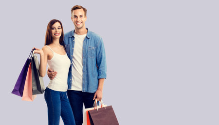 Holiday sales, shop, retail, consumer bank credit concept - happy couple with shopping bags, standing close to each other, and looking at camera. Grey background.の写真素材
