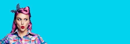 Excited surprised woman. Pinup girl looking sideways. Purple head model at retro fashion and vintage concept. Aqua blue color background. Copy space for some text or imaginary. Wide banner composition.の写真素材