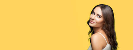 Portrait studio image of smiling young beautiful woman in white casual clothing, isolated against yellow color background. Copy space empty area for some advertising text or slogan.の写真素材