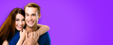 Smiling young amorous couple. Portrait image of embracing caucasian models at happy in love studio concept, against violet purple color background. Man and woman posing together, with copy spaceの写真素材