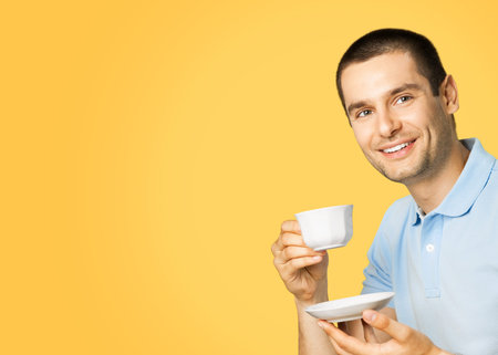 Portrait of young happy smiling man in blue casual clothing drinking coffee, isolated over yellow orange color background.の写真素材