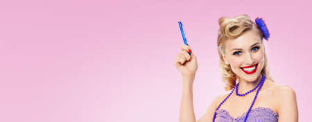 Portrait of beautiful young happy smiling woman in pin up style, showing some product or copy space area for text, over rose pink color background. Blond girl in retro fashion vintage studio concept.の写真素材