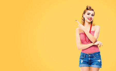 Happy smiling woman pointing at something. Excited girl in pin up, showing product or copy space for...